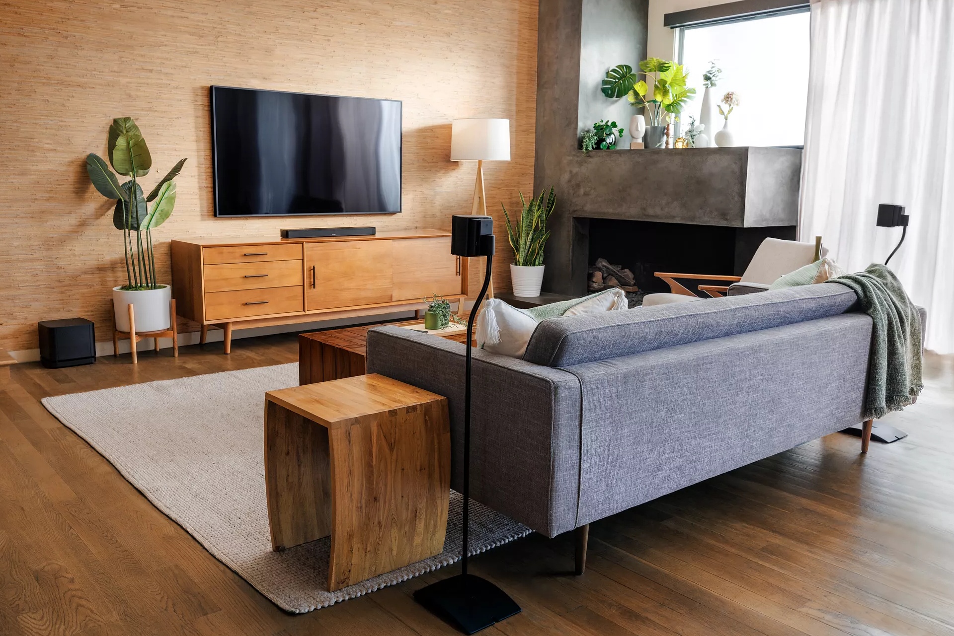 Un cinéma maison dans un salon avec une barre de son Bose sur un meuble télé, enceintes ambiophoniques derrière le canapé et un module de basses 700 à côté d’une plante