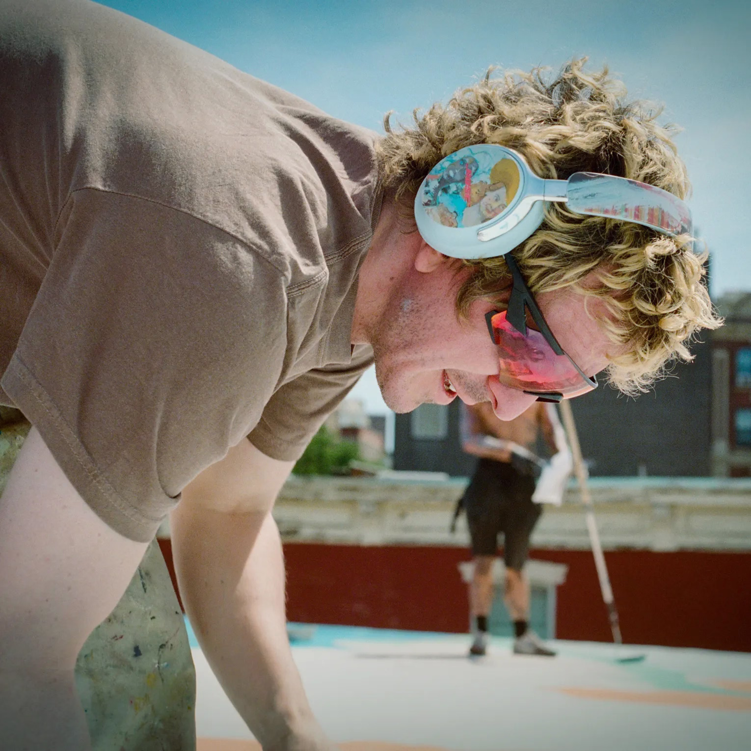 KidSuper wearing Moonstone Blue Bose &times; KidSuper QuietComfort Ultra Headphones (2nd Gen) hand painting the rooftop of a city building.
