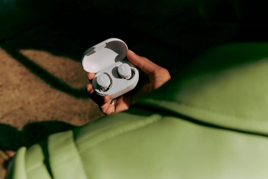 A person holding a pair of Bose QuietComfort Earbuds in their charging case.