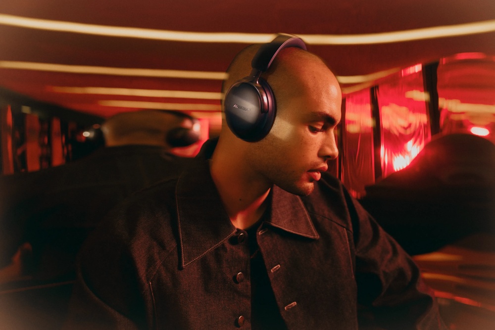 A man wearing black QuietComfort Ultra Headphones in a room with mirros and lights