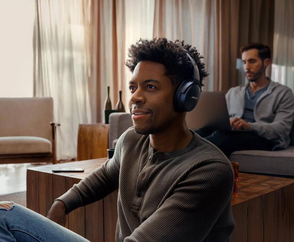A man watching TV and listening through QuietComfort 45 Headphones using SimpleSync