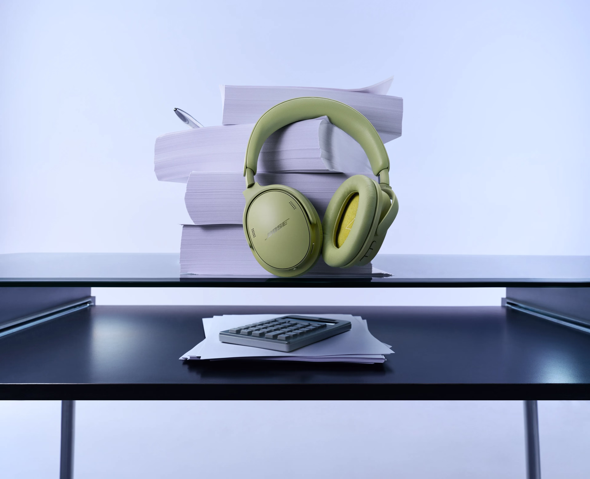 Bose QuietComfort Headphones (2nd Gen) in Eucalyptus Green displayed on a desk beside stacked books and office supplies.