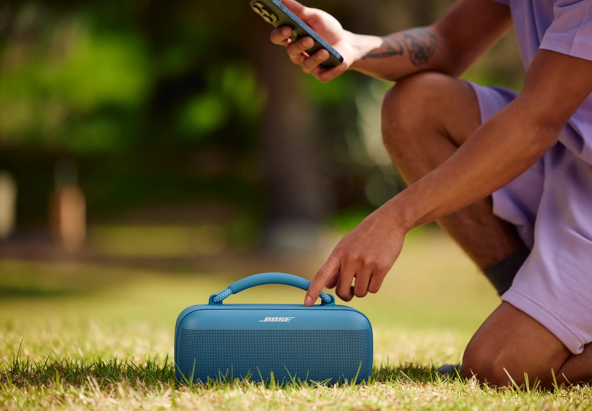 Person outside kneeling next to a Bose SoundLink Max Portable Speaker and adjusting volume.