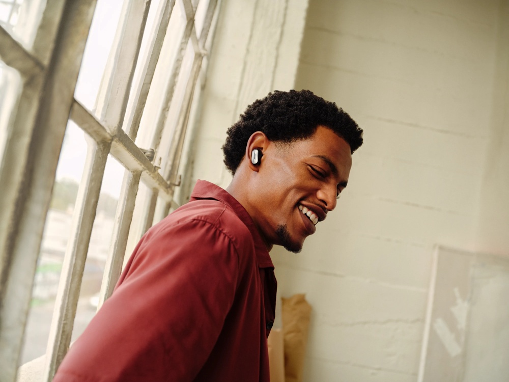 A man smiling indoors while using black Bose QuietComfort Ultra Earbuds (2nd Gen).