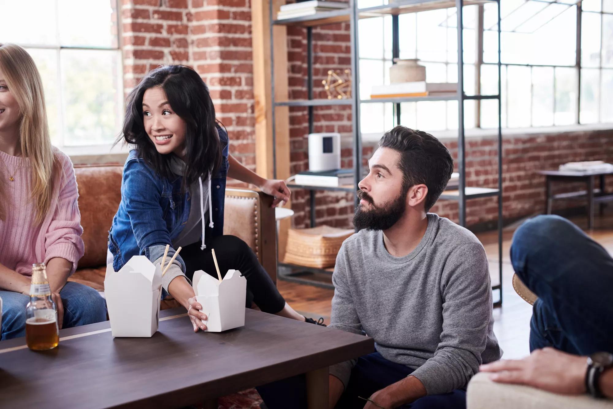 A group of friends sit in a living room and enjoy takeout 