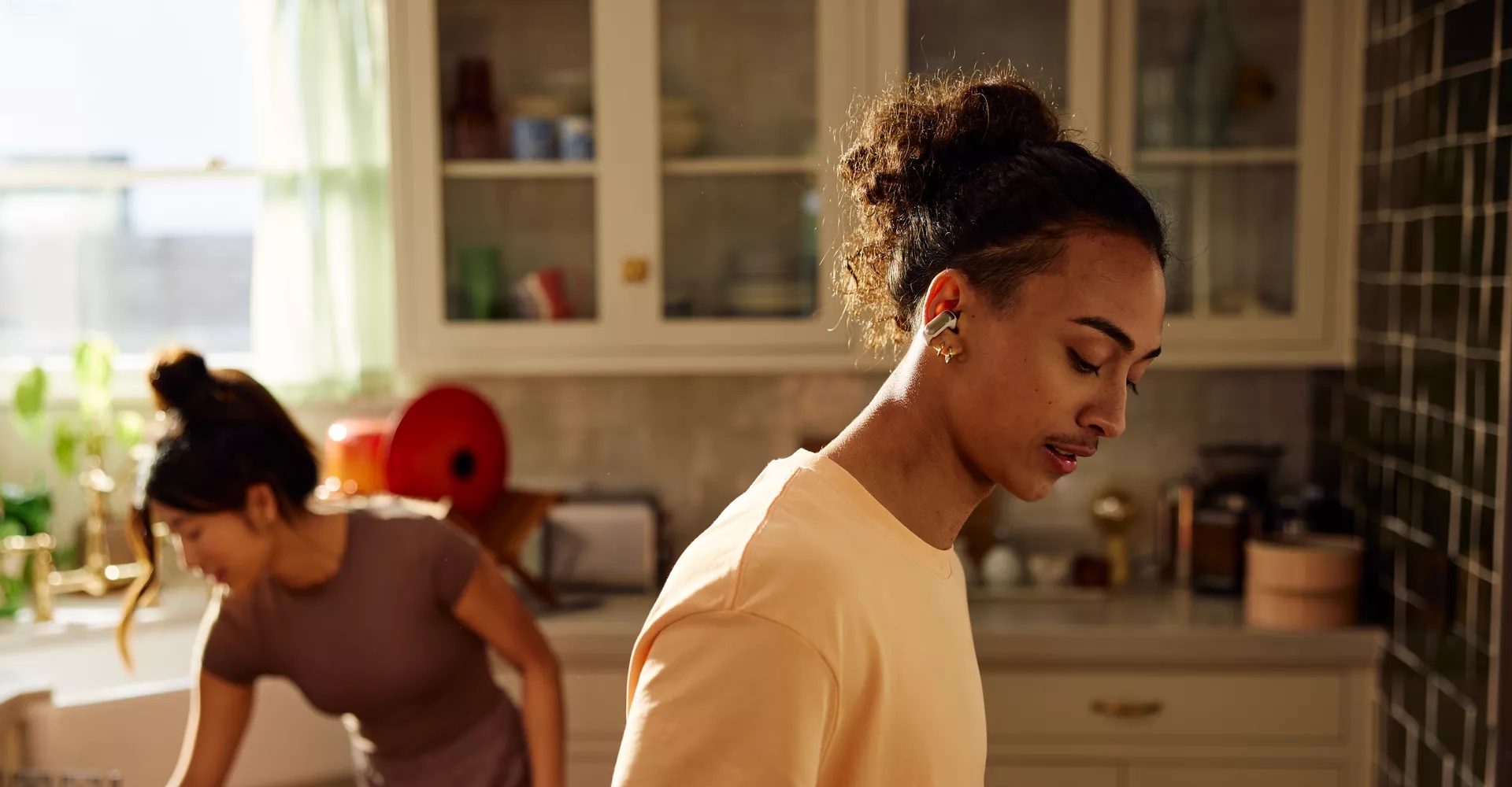 Man wearing Bose Ultra Open Earbuds while cleaning the kitchen with his wife