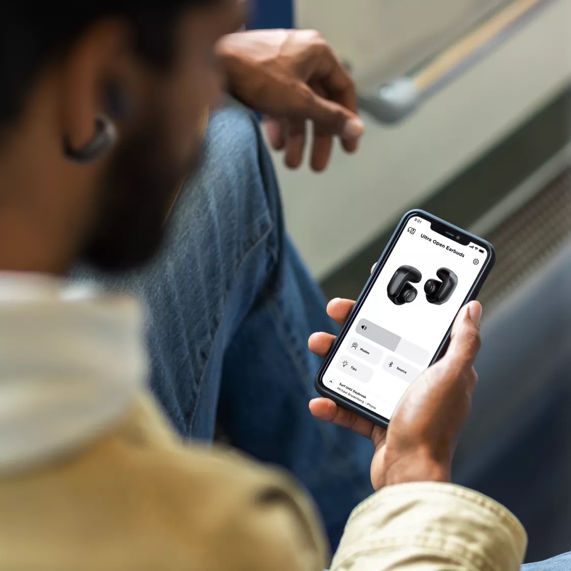 Man sitting on a train using the Bose app to adjusting his Bose Ultra Open Earbuds