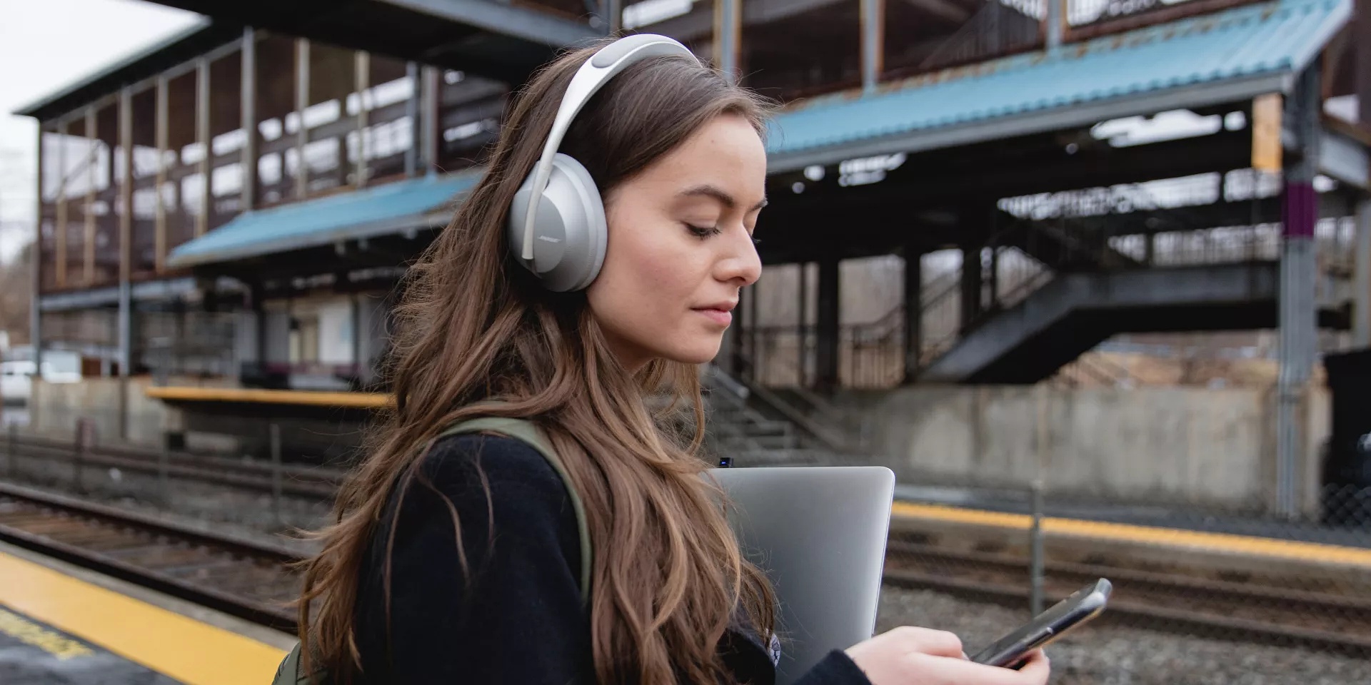 Woman waiting for train and fixing Noise Cancelling Headphones 700 app issue