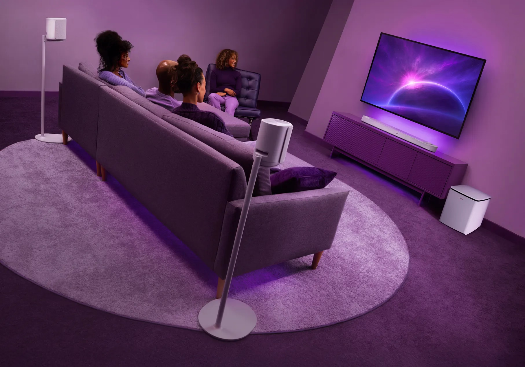 Friends sitting in a living room watching TV with a Bose Lifestyle Ultra Soundbar, Lifestyle Ultra Speakers on floor stands, and Lifestyle Ultra Subwoofer.