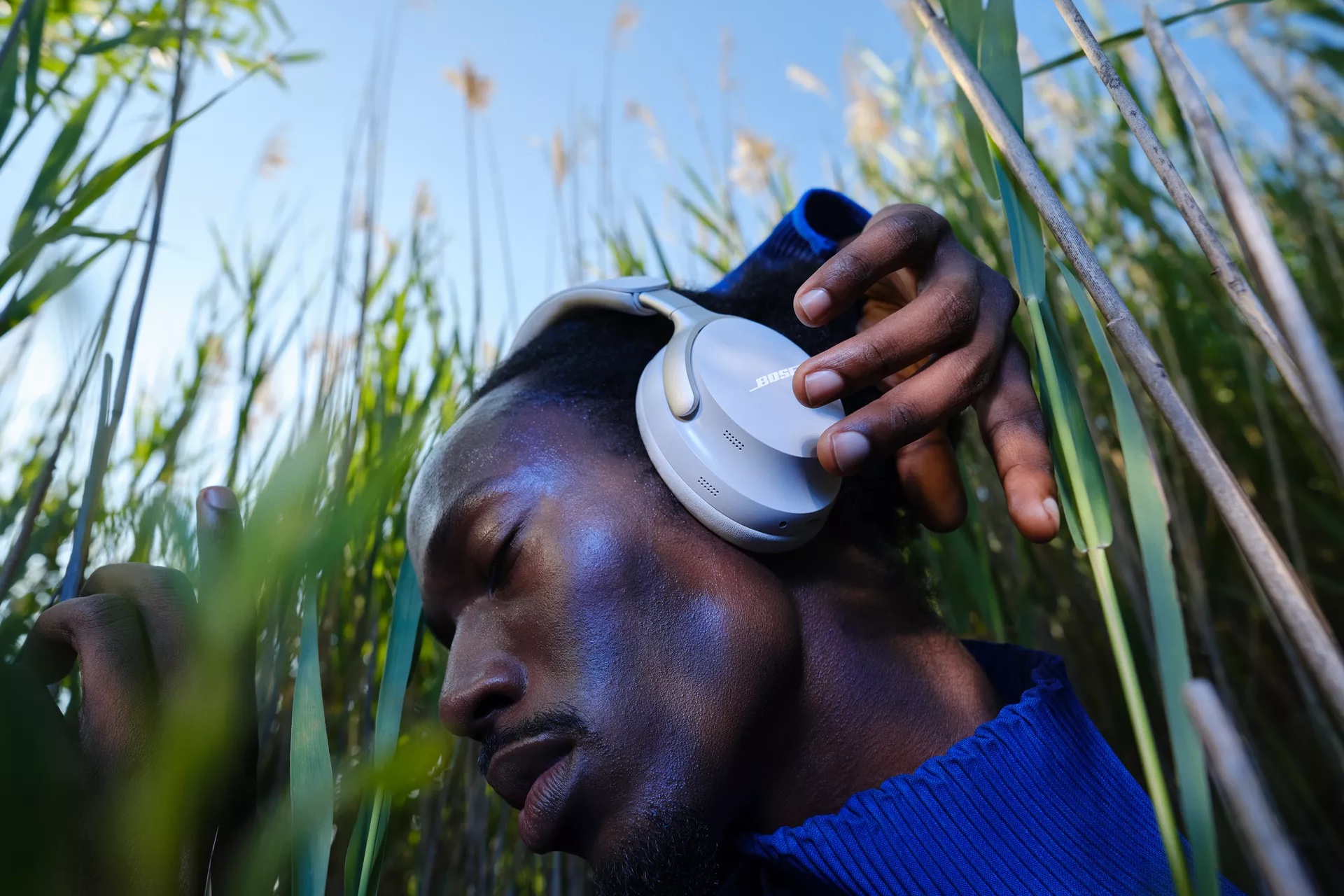 Un homme debout dans des herbes hautes qui ajuste un casque QuietComfort Ultra