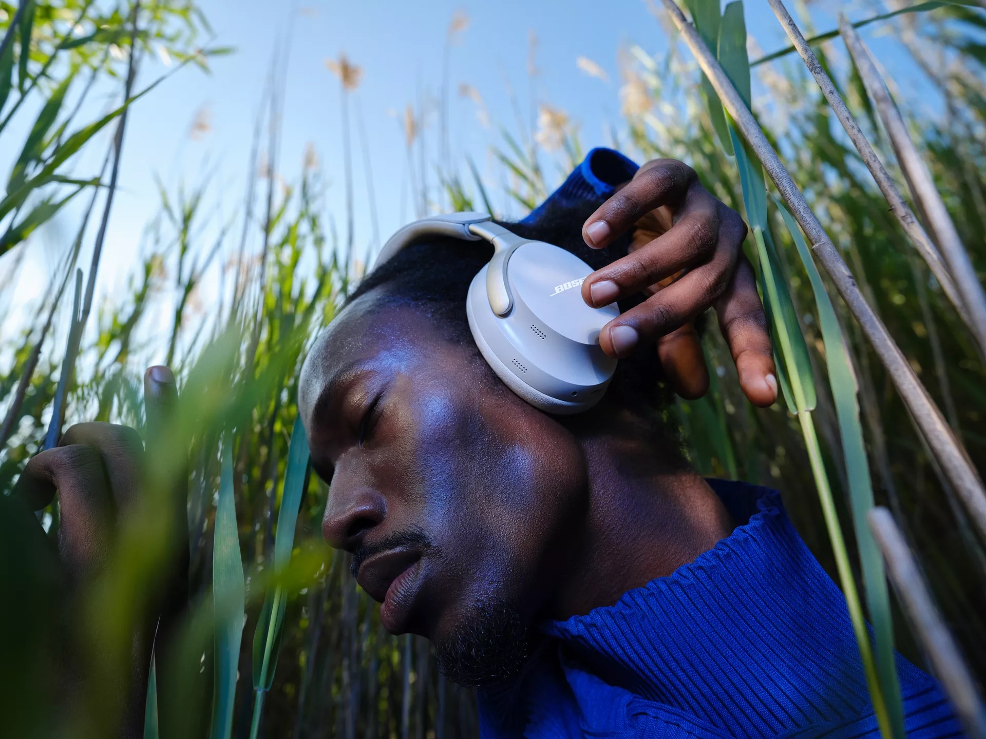 Guy standing in tall grass and adjusting QuietComfort Ultra Headphones
