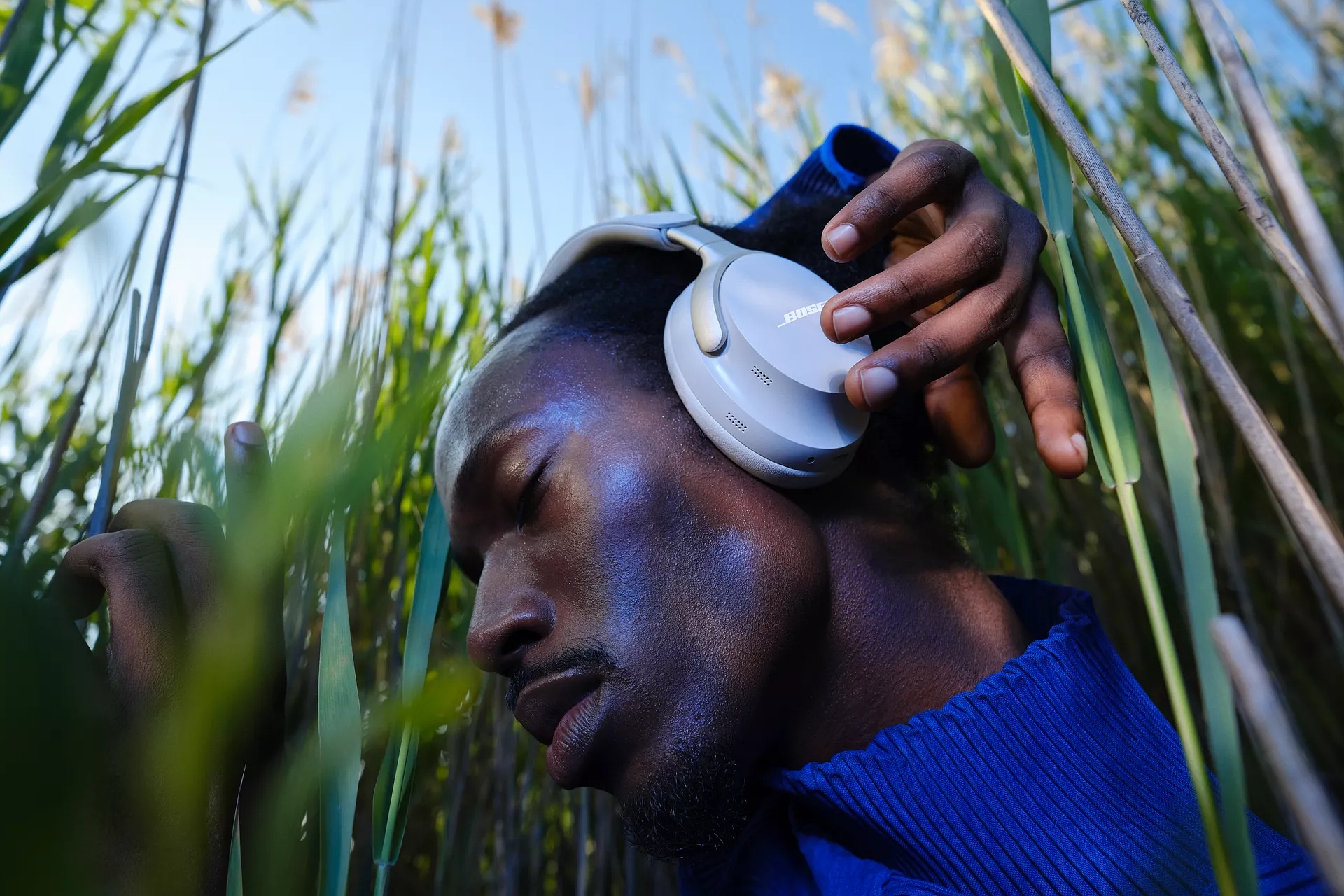 Guy standing in tall grass and adjusting QuietComfort Ultra Headphones