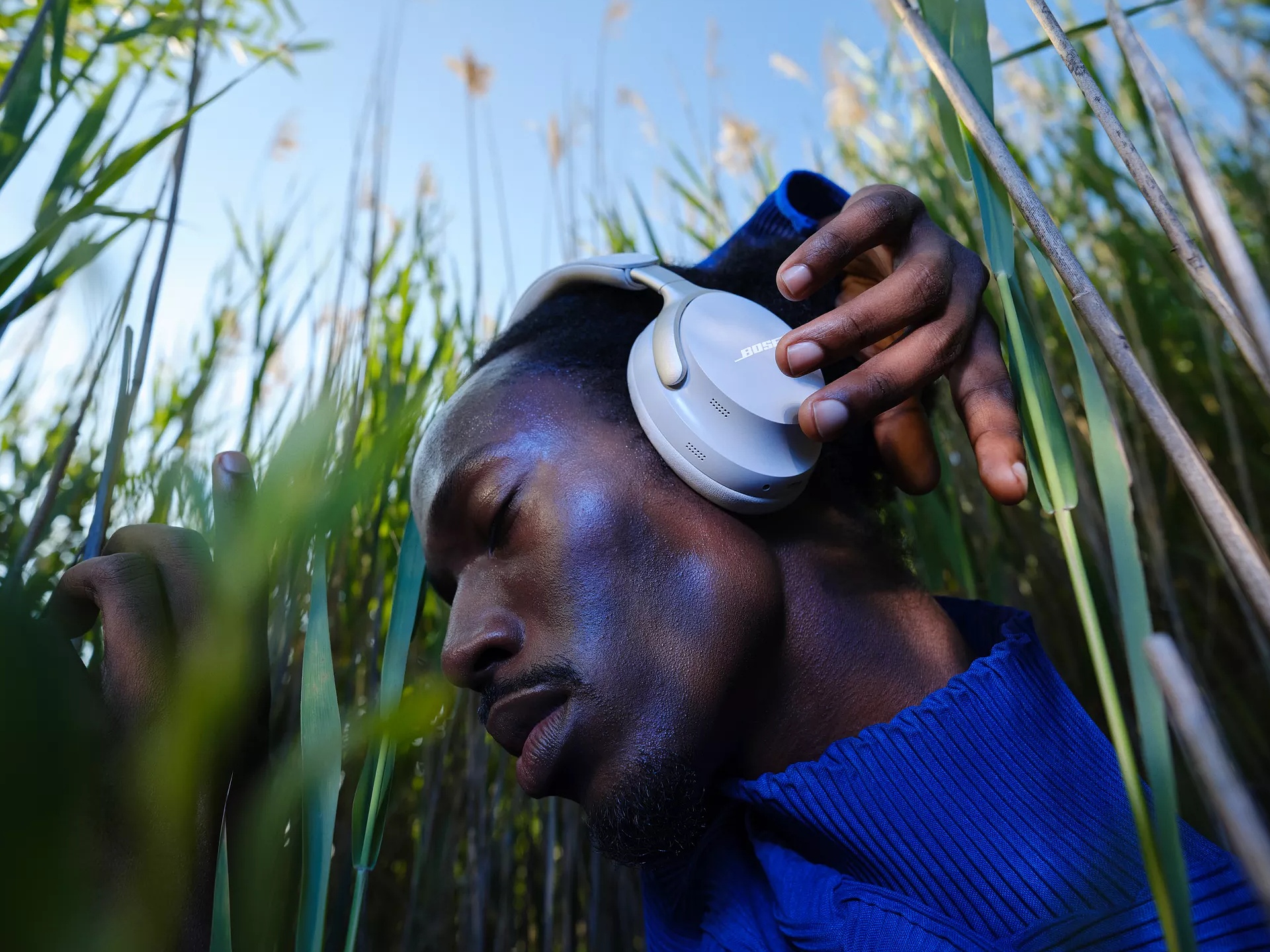 Guy standing in tall grass and adjusting QuietComfort Ultra Headphones