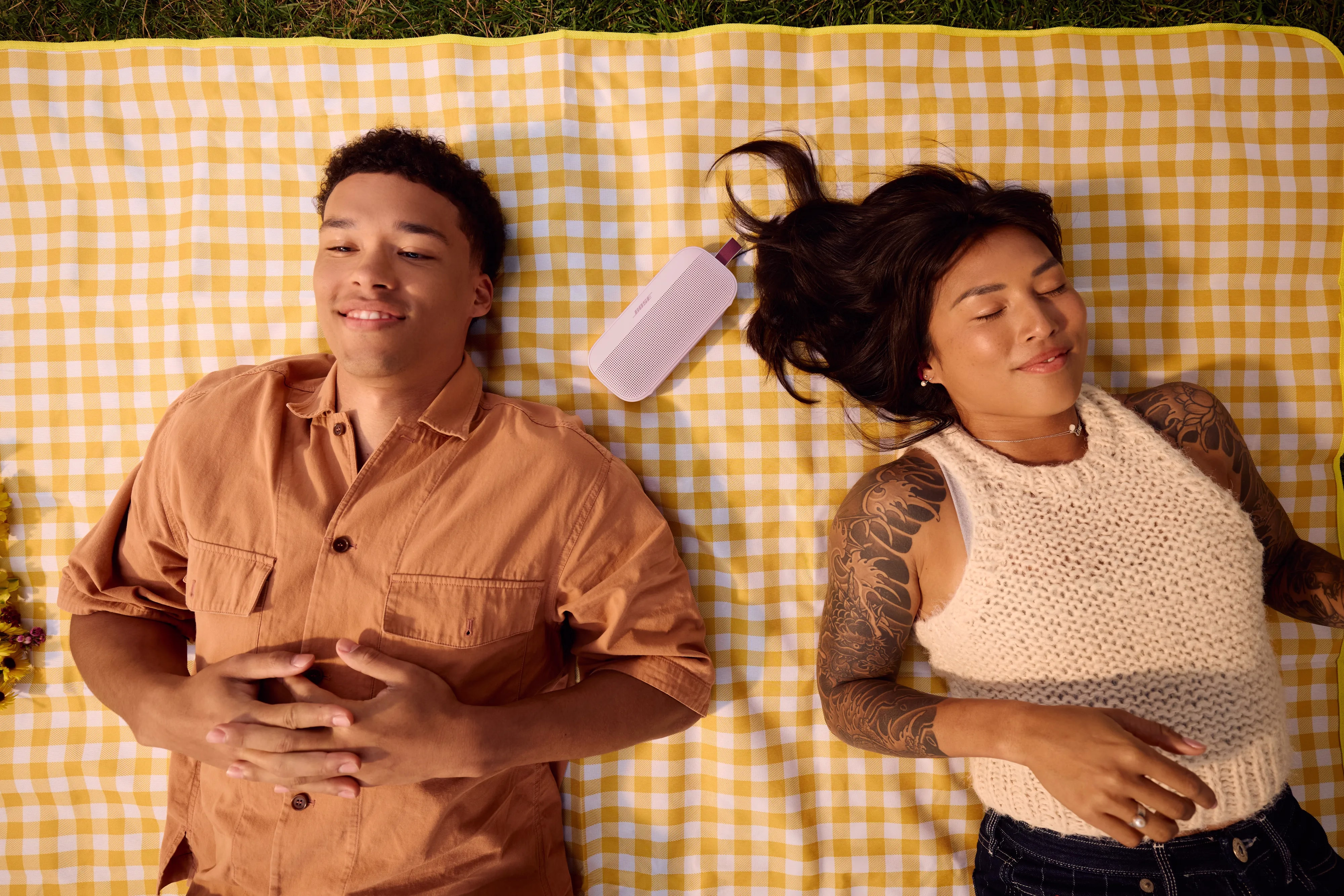 Couple laying on a blanket with a Bose SoundLink Flex Portable Speaker (2nd Gen) in between their heads.