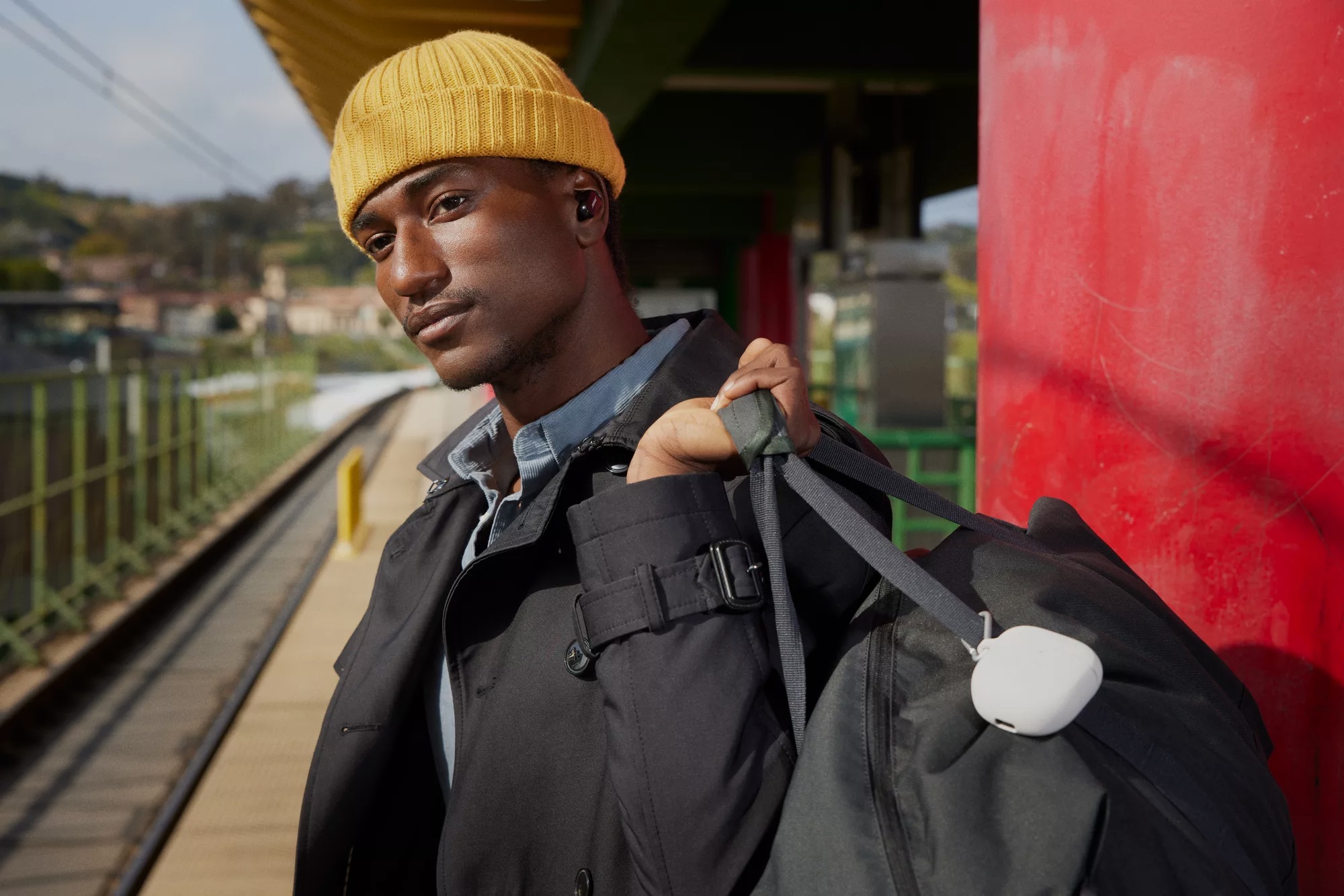 Gentleman waiting for train listening to QuietComfort Earbuds II and holding bag with Carrying Case attached