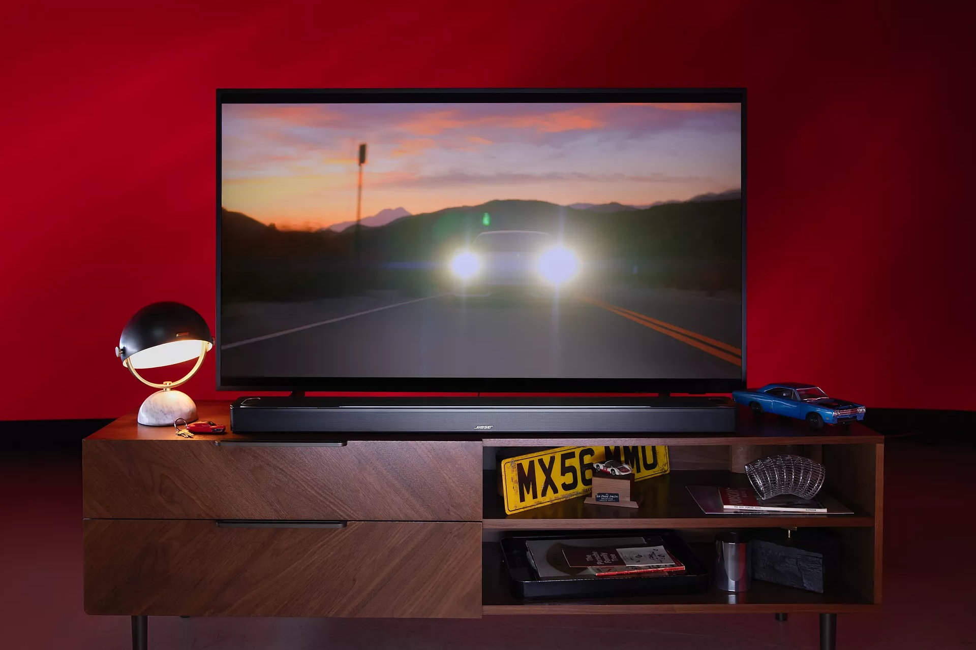 Barre de son intelligente Bose Ultra sur un meuble télé pendant qu’un film avec une voiture est diffusé à la télévision