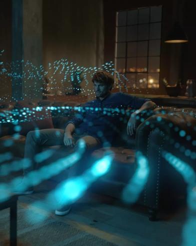 Man in a living room watching TV with sound waves radiating from the speaker system showing the effects of Dolby Atmos