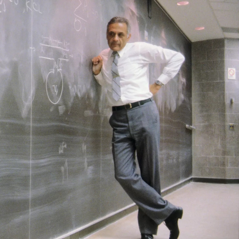 Dr Amar Bose in a classroom leaning against a chalkboard