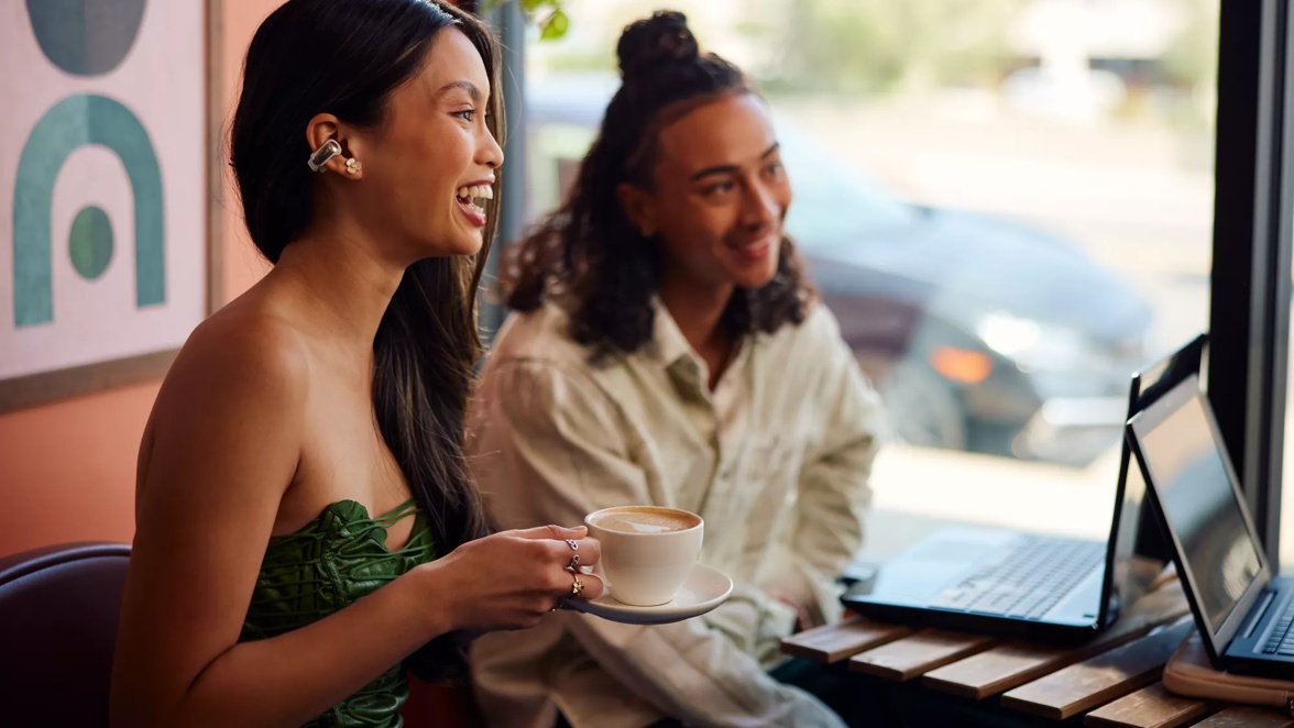 Woman wearing Bose Ultra Open Earbuds in a cafe with friends having coffee.