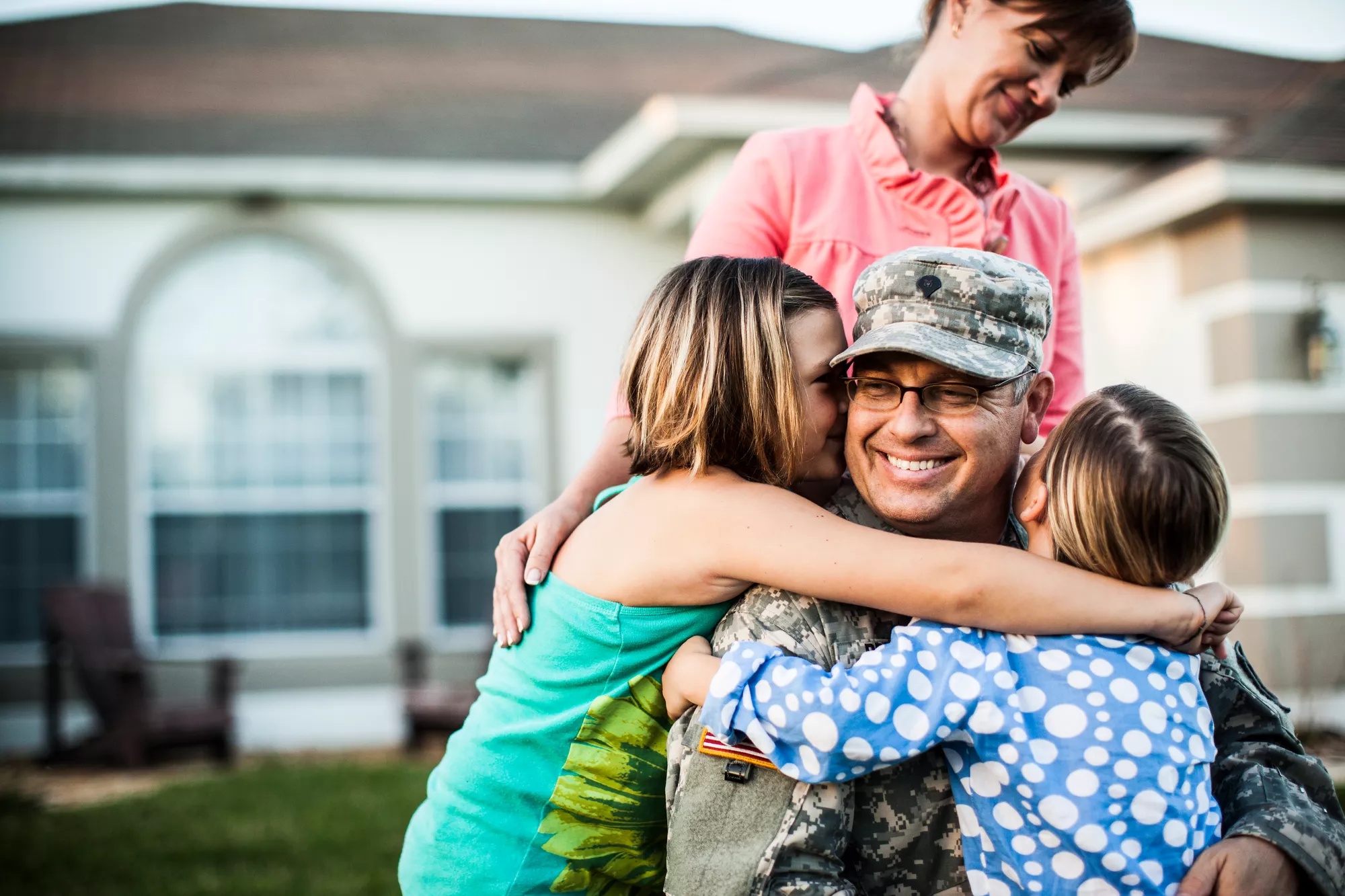 Soldier being hugged by his 2 children with his wife watching.