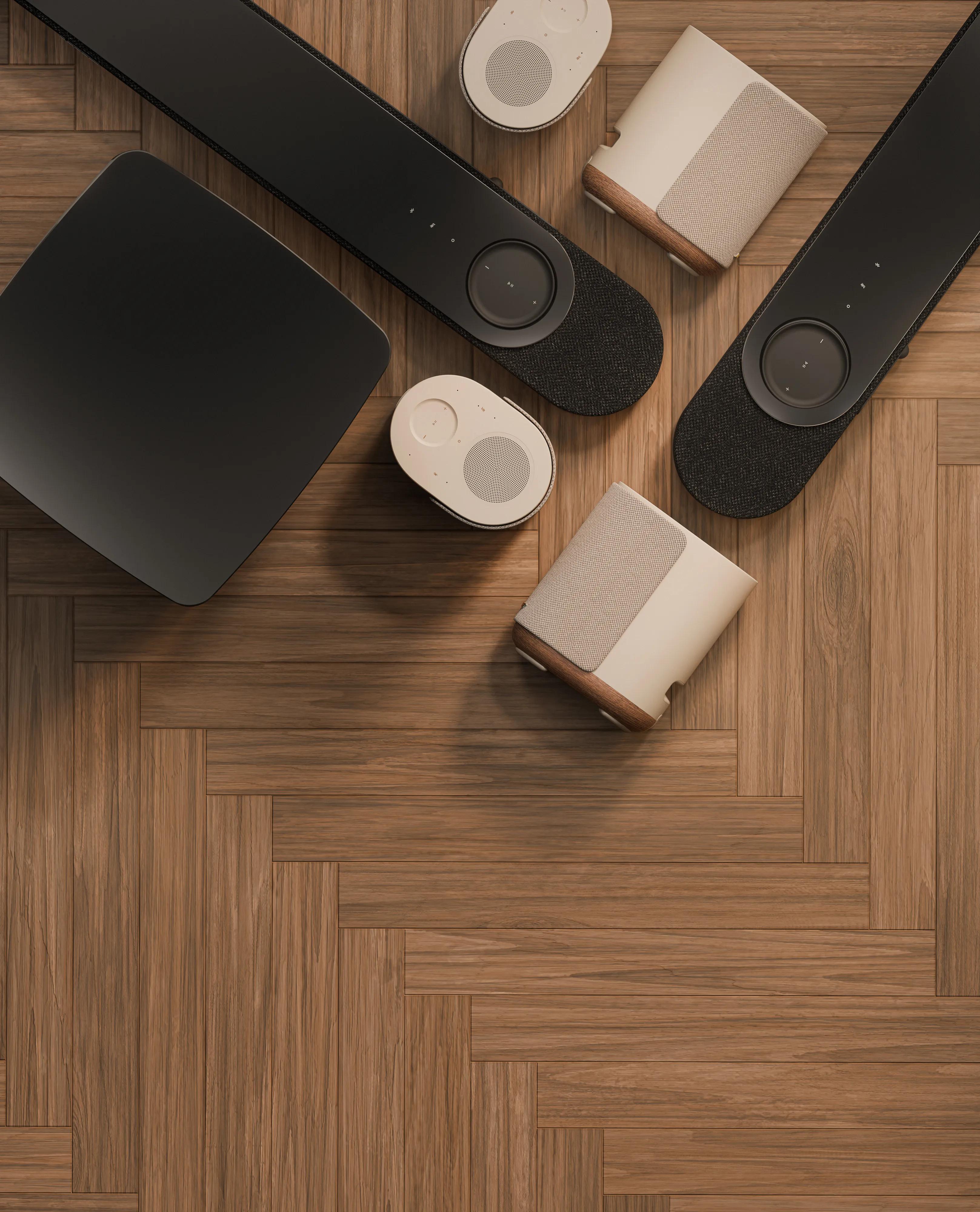 Bose Lifestyle Ultra Soundbar, Lifestyle Ultra Speakers, and Lifestyle Ultra Subwoofer home audio system in Nue Black and Driftwood Sand arranged on a wooden floor.