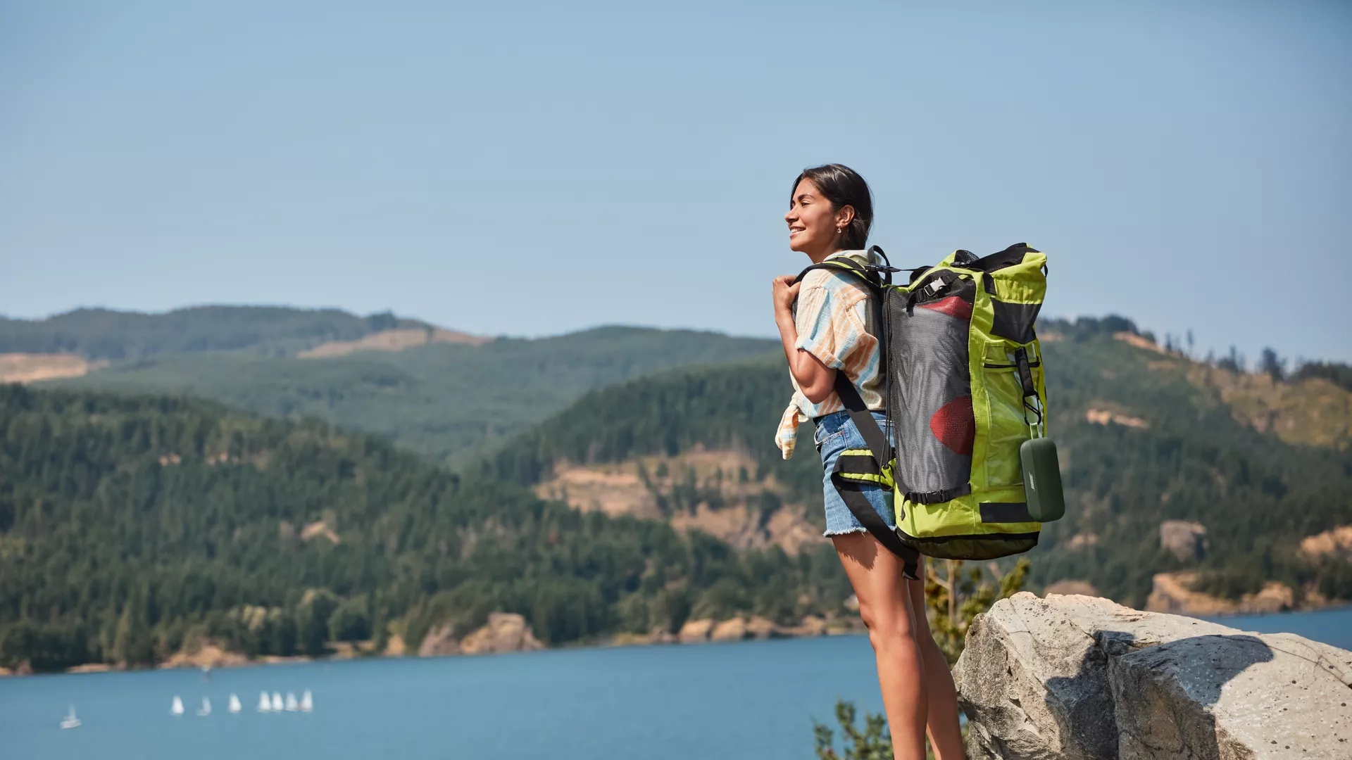 Femme faisant de la randonnée avec une enceinte Bluetooth SoundLink Flex couleur vert cyprès attachée à son sac à dos