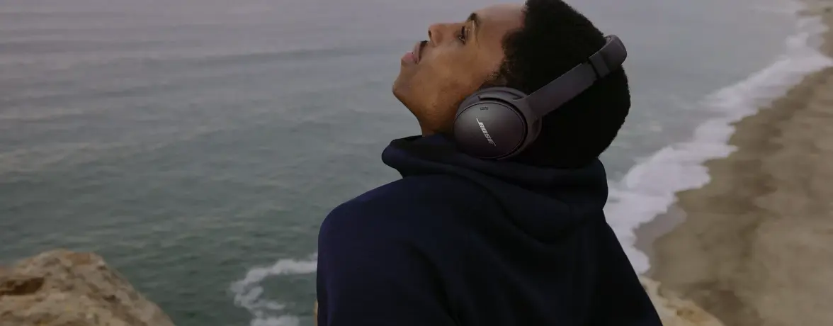 Man at the beach relaxing with QuietComfort 45 headphones 