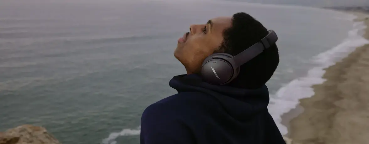 Man at the beach relaxing with QuietComfort 45 headphones