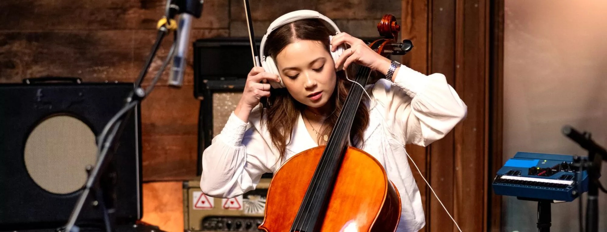 Laufey adjusting her Bose QuietComfort Ultra Headphones while holding a cello