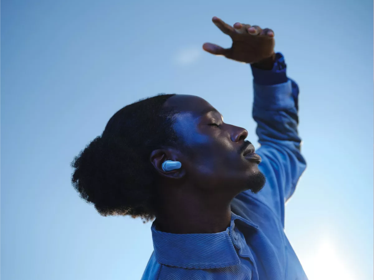 Homme portant les écouteurs QuietComfort Ultra à l’extérieur, sur arrière-plan de ciel bleu dégagé