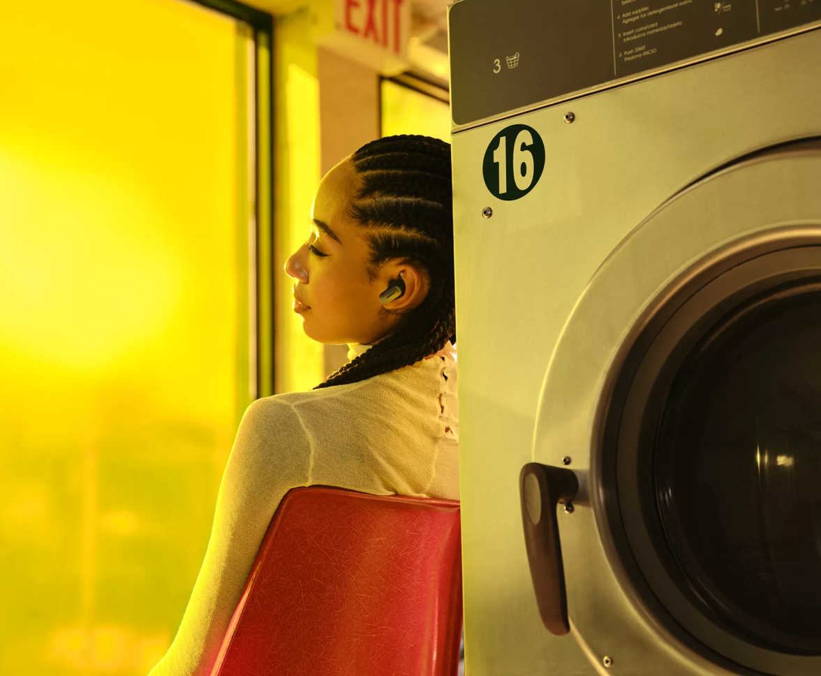 Person sitting in a laundromat wearing Bose QuietComfort Ultra Earbuds