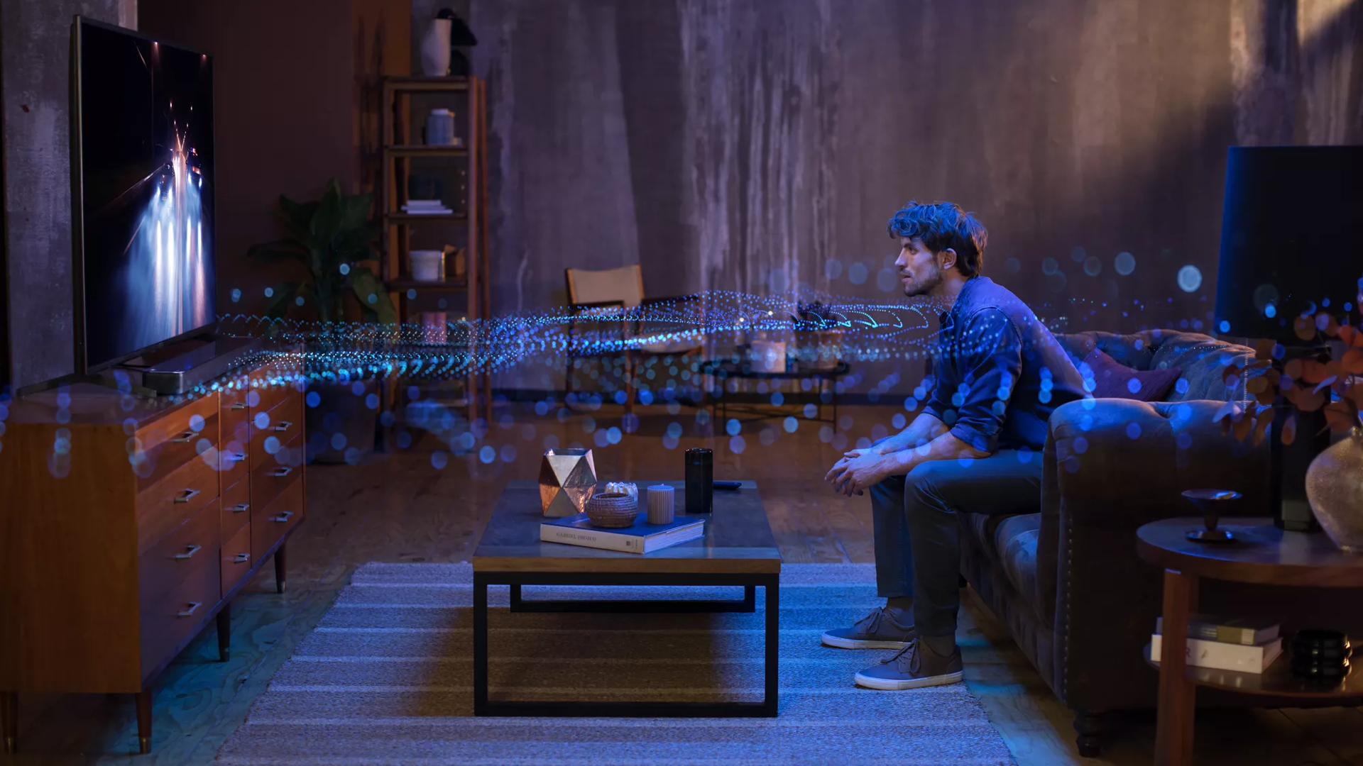 Man in a living room watching TV with sound waves radiating from the speaker system showing the effects of Dolby Atmos