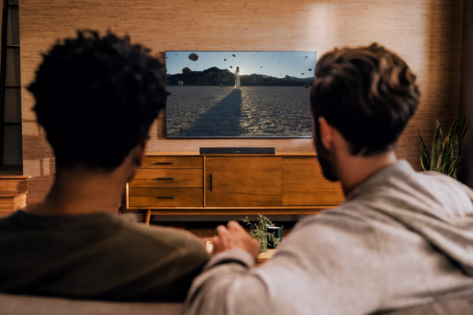 Two guys sitting on couch, watching a movie, and experiencing Dolby Atmos through a Bose Soundbar