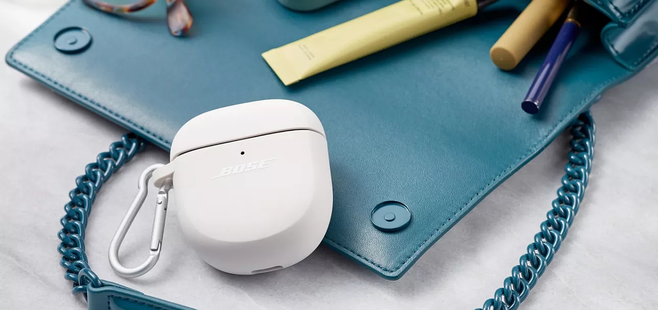 Étui en silicone pour écouteurs QuietComfort II protégeant le boîtier des écouteurs à l’intérieur d’un sac à main contenant du maquillage et des lunettes.