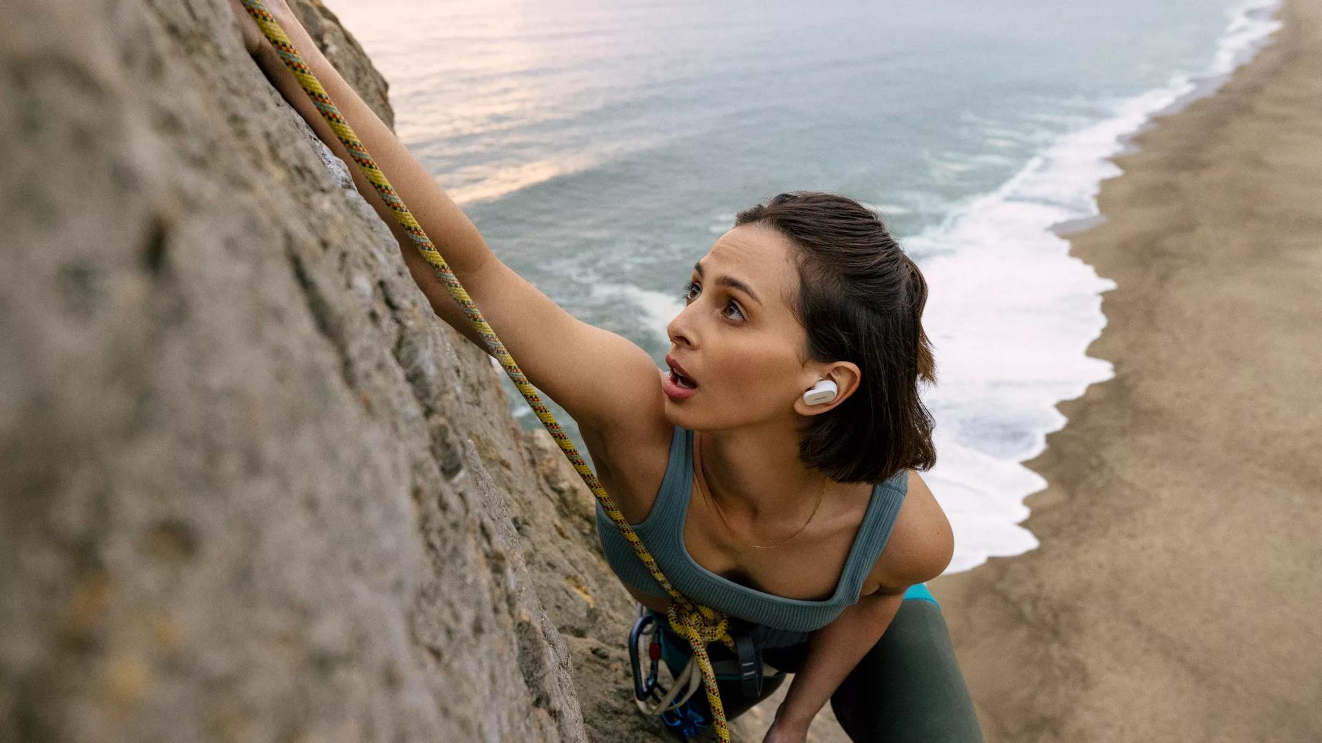 Une femme portant les &eacute;couteurs QuietComfort&nbsp;II en faisant de l&rsquo;escalade pr&egrave;s de l&rsquo;oc&eacute;an