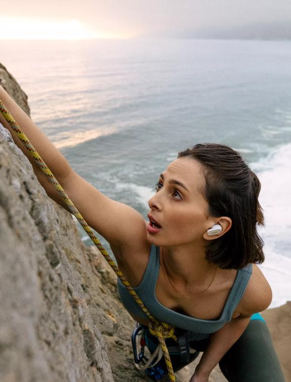 Woman wearing Bose QuietComfort Earbuds II while rock climbing near the ocean