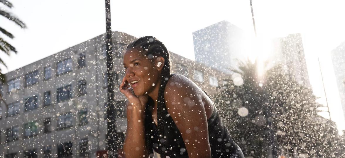 Woman wearing Bose QuietComfort Earbuds II outside with water being splashed on her