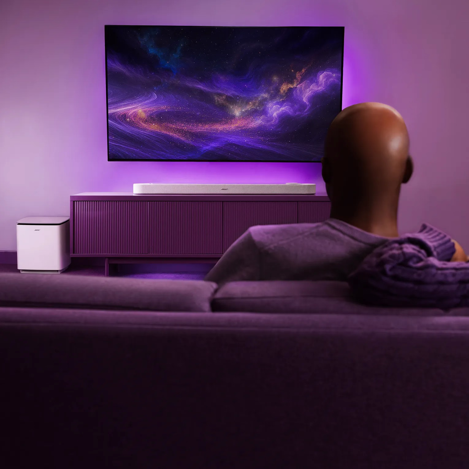 Bose Lifestyle Ultra SoundbarとLifestyle Ultra Subwooferを設置したリビングルームでくつろいでテレビを楽しむ男性。
