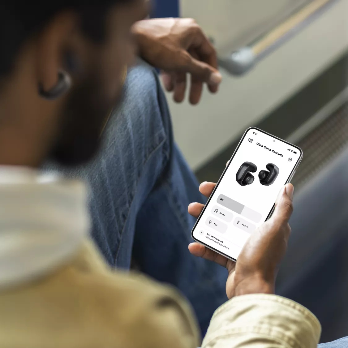 A man using the Bose App on his smartphone to control his Bose Ultra Open Earbuds.