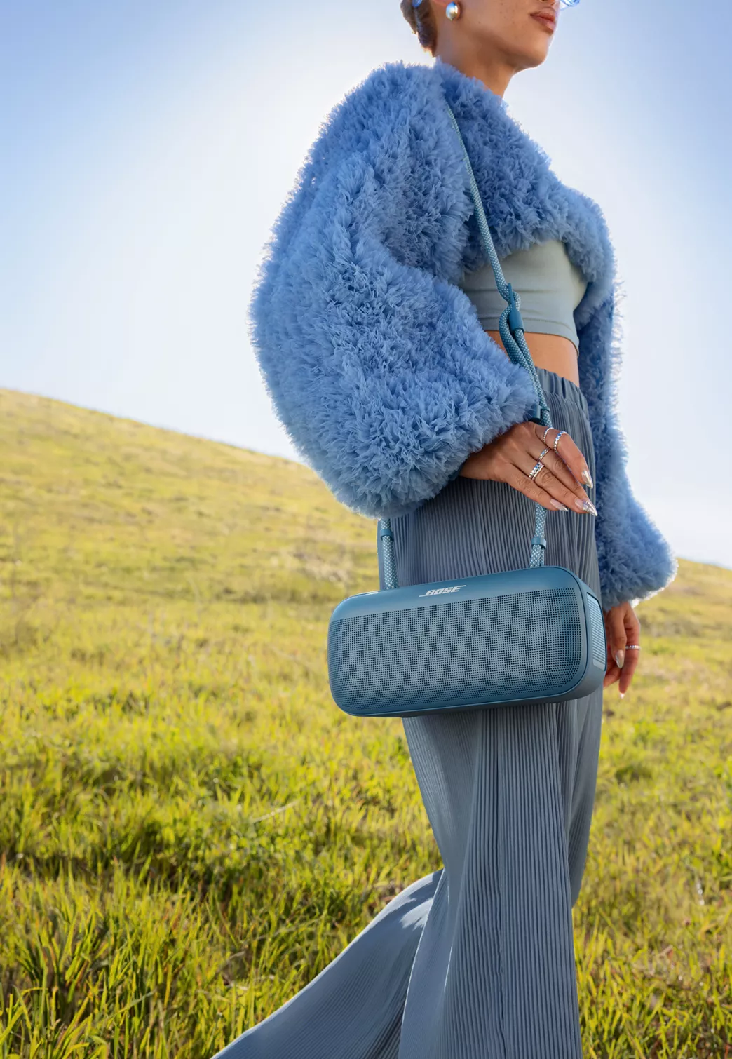 Femme transportant une enceinte portative Bose SoundLink Max avec une courroie de transport en corde Bleu brunante