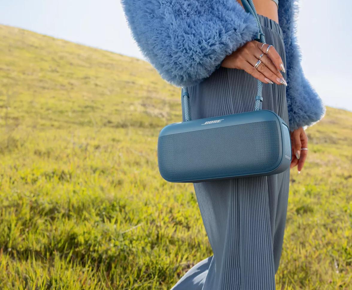 Young woman carrying a Bose SoundLink Max Portable Speaker through a field using the Rope Carrying Strap