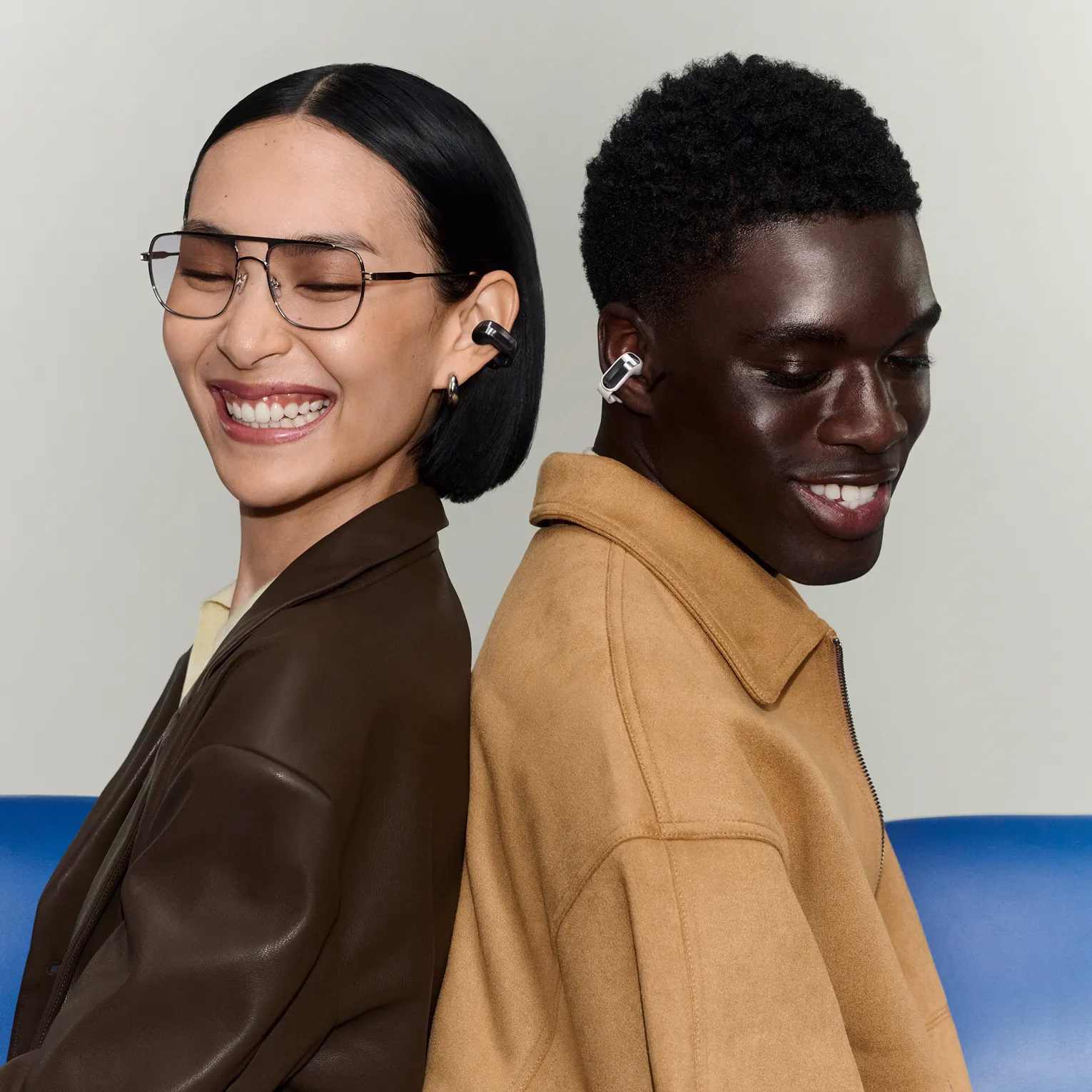 Woman wearing Bose Ultra Open Earbuds (2nd Gen)in Black standing back to back with a man wearing Bose Ultra Open Earbuds (2nd Gen) in While Smoke.