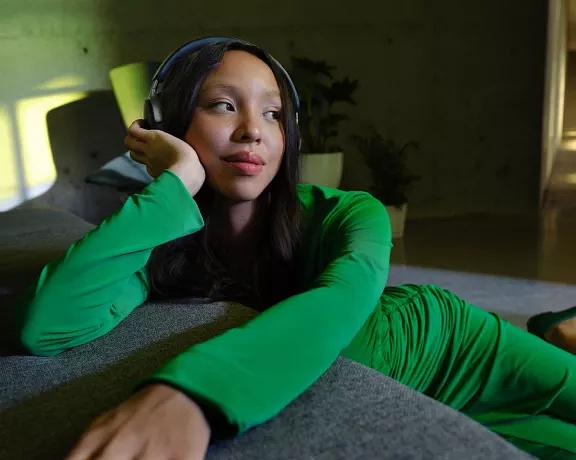 Girl sitting on floor and leaning on couch listening to QuietComfort Ultra Headphones