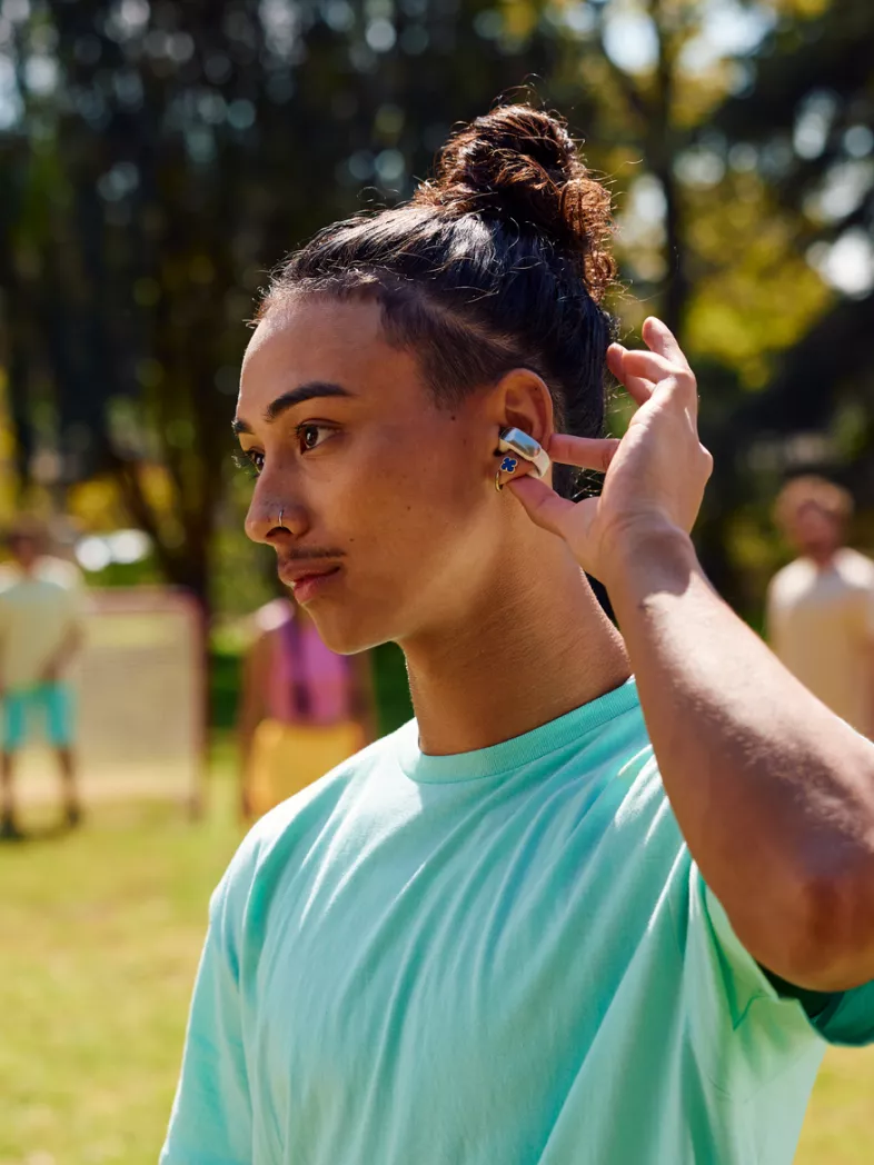Young man listening to music, using the touch controls of the Bose Ultra Open Earbuds while playing soccer