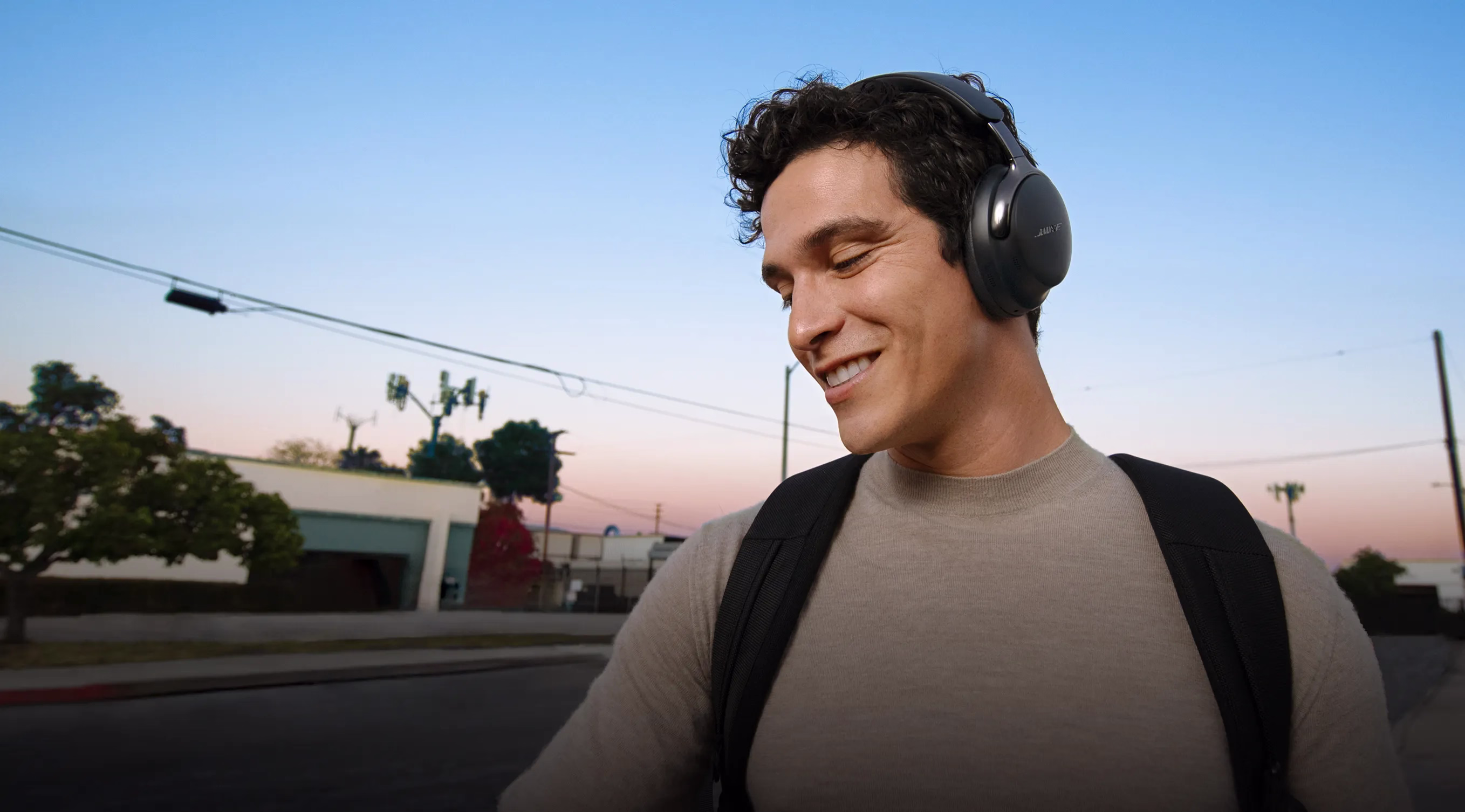 A young man walking outside with a backpack wearing Bose QuietComfort Ultra Headphones (2nd Gen).