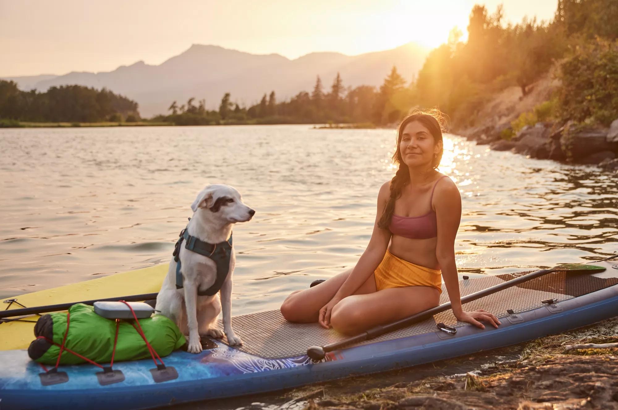 Ana Alarc&oacute;n and her dog sitting on her paddleboard by a lake with a SoundLink Flex Bluetooth speaker attached to her backpack