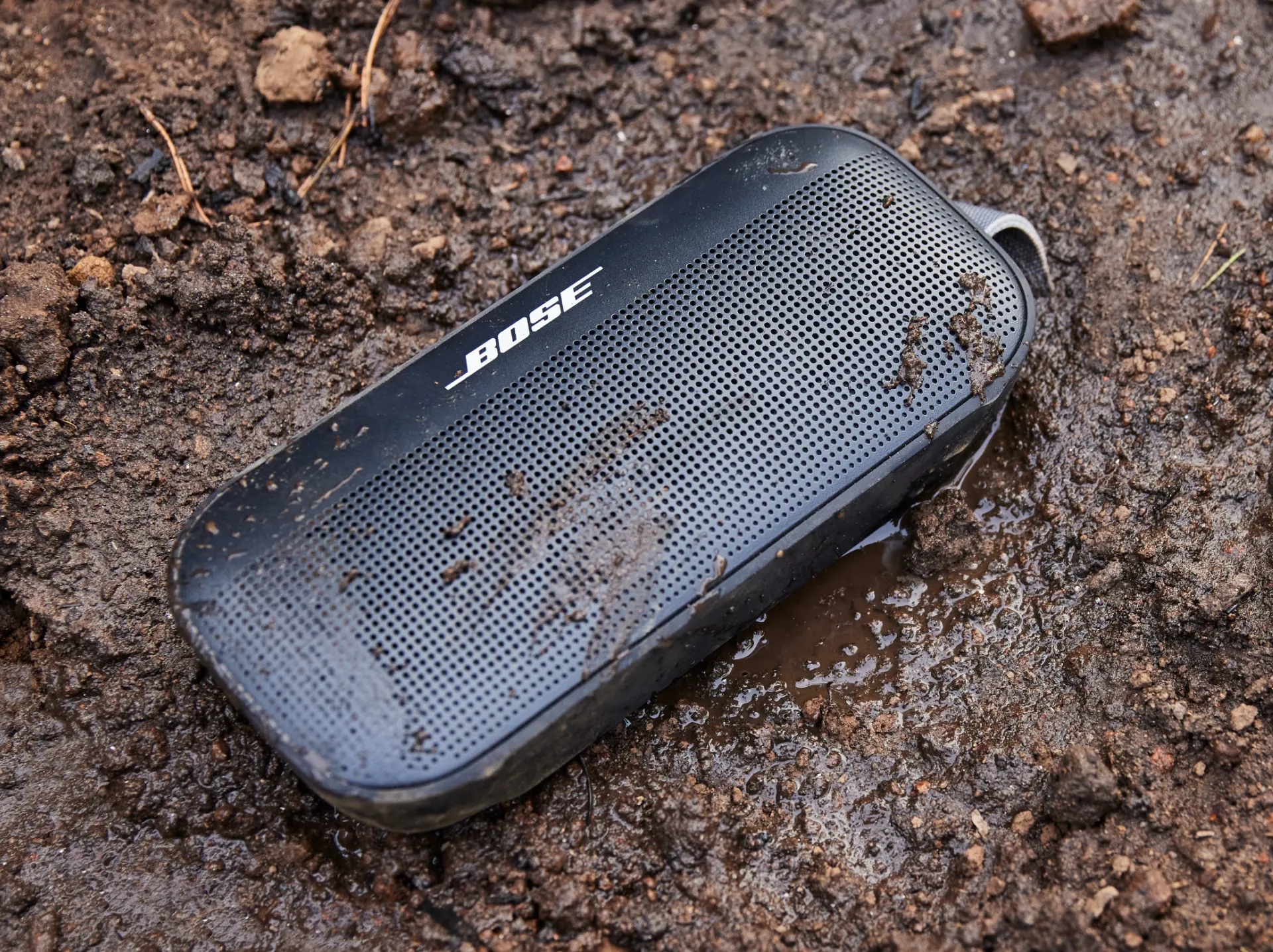 Une enceinte Bluetooth Bose SoundLink Flex posée sur le sol avec de l’eau et de la boue dessus