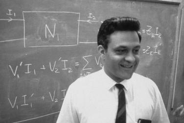 Dr. Amar Bose stands in front of a chalkboard