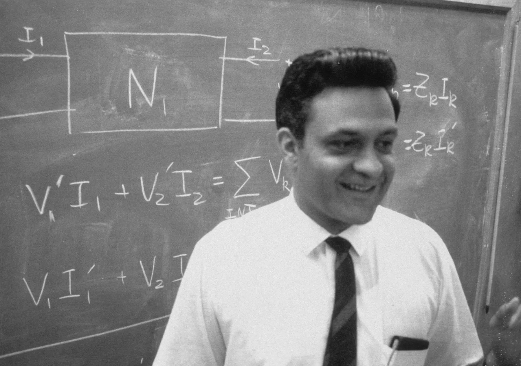 Dr. Amar Bose stands in front of a chalkboard
