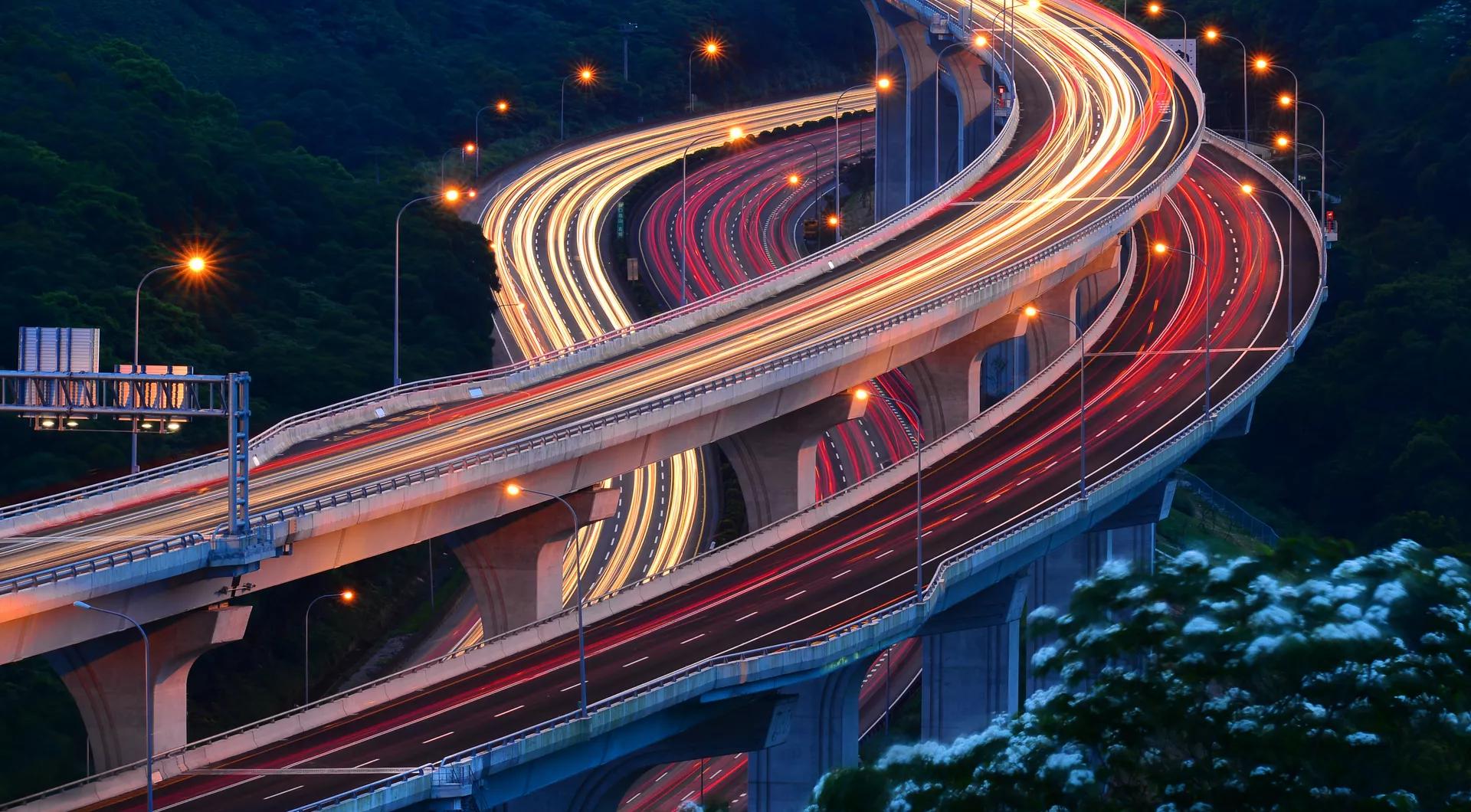 Three winding highway overpasses and underpasses at night with the traffic lights in motion. 